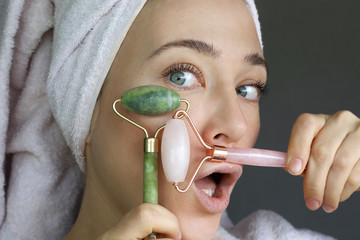 Woman making massage with pink and green jade roller. Beauty tools for face treatment. Funny face.