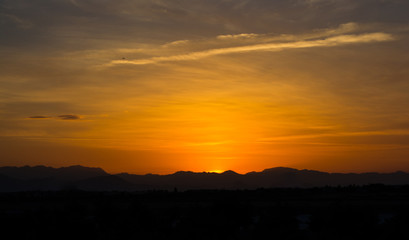 View of golden sky with the mountain silhouette in the time of lovely sunset over a city.
