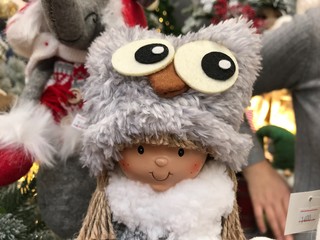 Portrait of a doll in a gray hat in the form of an owl on the background of other toys and customers in the store. Mobile photo with shop lighting