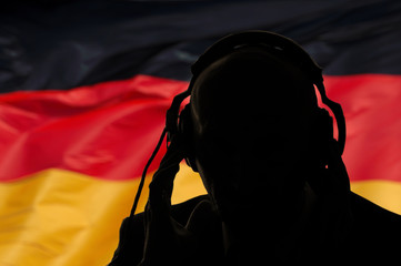 Silhouette of a man in headphones on the background of the flag of Germany, eavesdropping...