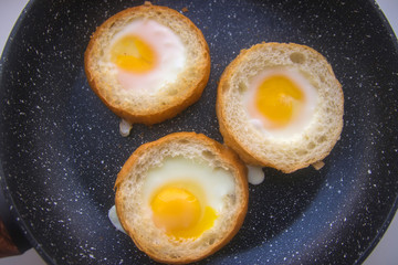 three eggs baked in round buns in a dark pan top view close-up