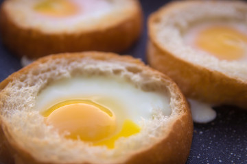 three eggs baked in round buns in a dark pan top view close-up
