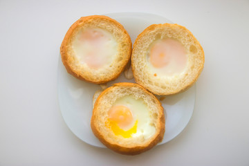 three eggs baked in round buns on a white plate on a white kitchen table top view close-up