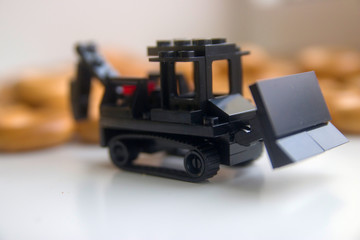 black toy bulldozer made of designer cubes on a background of bagels close-up