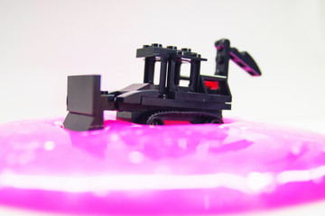 black toy bulldozer from designer cubes removes pink gel with glitter on a white background