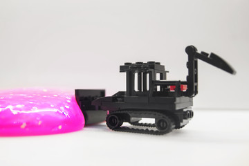 black toy bulldozer from designer cubes removes pink gel with glitter on a white background