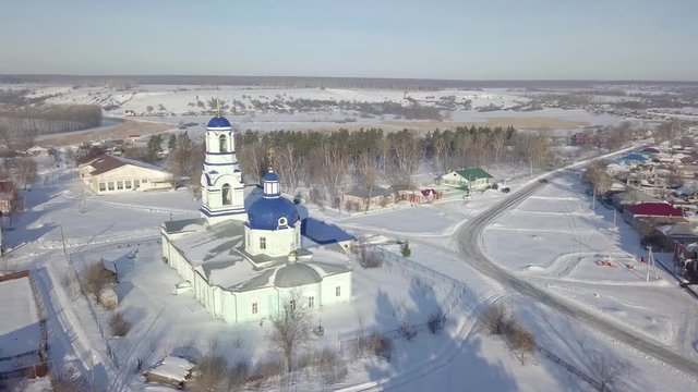Aerial view of local orthodox church in Russian village with blue domes and golden crosses in sunny winter day. Shot. Religion and faith