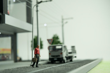 Selective focus of doll figure adult man walking across street with blurred background. Road safety concept.