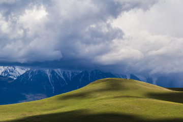 Fototapeta premium Mountainous countryside with green meadows dark clouds and snow capped cliffs
