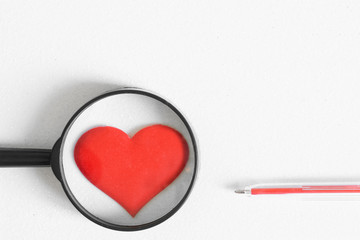 A red heart under a magnifying glass next to a red fountain pen. Health topics and the choice of a loved one