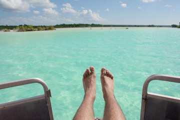 Men feet and legs on a sailboat traveling on the caribbean sea near the coastline