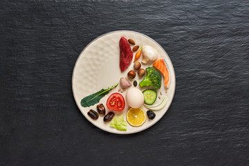16:8 fasting diet concept. Two third plate with healthy food and one third plate is empty. Beef, salmon, egg, broccoli, tomato, nuts, carrots, mushrooms, cucumber, dates. Dark background Copy space. 