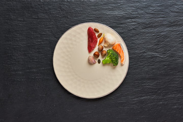 20:4 fasting diet concept. One third plate with healthy food and two third plate is empty. Beef, salmon, egg, broccoli, tomato, nuts, carrots, mushrooms, cucumber, dates., cutlery Dark background Cop
