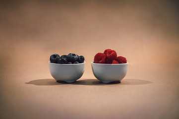 Raspberries and blueberries in white bowls with rustic background