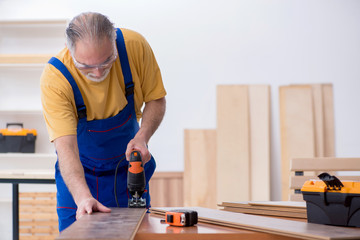Old male carpenter working in workshop