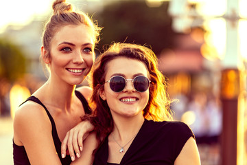 Close up portrait of young female couple. Two attractive girls looking aside while relaxing outdoors, admiring sunset. Lesbian lives, travel concept. Love is love. Horizontal shot. Selective focus