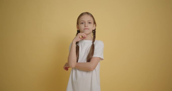 Little girl with braids make sarcastic pose at yellow background slow motion
