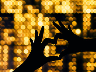 Silhouete two hand make heart shape over gold abstract blured background.