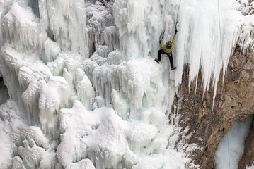 A solo male ice climber uses climbing equipment to work his way up frozen Upper Falls in Johnston Canyon