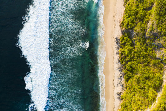 View from above, stunning aerial view of a rocky shore with a beautiful beach bathed by a rough sea during sunset, Nyang Nyang Beach (Pantai Nyang Nyang), South Bali, Indonesia. © Travel Wild