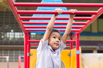 Obraz premium Kid exercise for health and sport concept. Happy Asian student​ child boy playing and hanging from a steel bar at the playground. 5 years old.