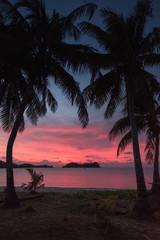 Malakati village, Fiji - 10/26/2019: Colourful sunset with palm trees over the ocean on a white sandy beach in Fiji