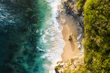 View from above, stunning aerial view of a rocky shore with a beautiful beach bathed by a rough sea during sunset, Nyang Nyang Beach (Pantai Nyang Nyang), South Bali, Indonesia.