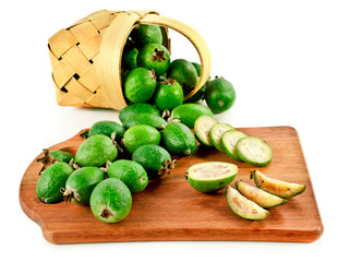Fresh feijoa fruits (acca sellowiana, pineapple guava) in the basket and sliced on wooden desk isolated on a white background.