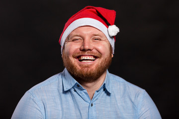 Laughing redhead man in a Santa hat. Close-up. Black background.