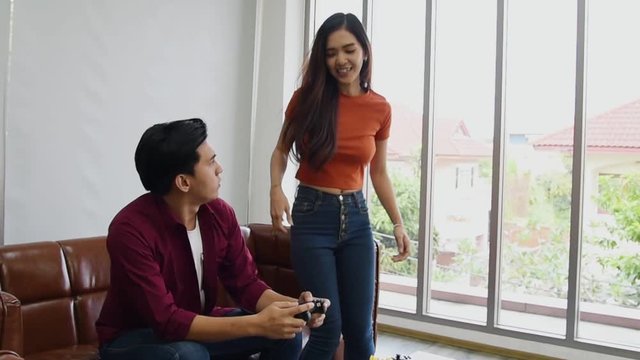 Young Asian couple sitting on couch and playing console video game together and his girlfriend get touchy  from him in holiday free time in living room