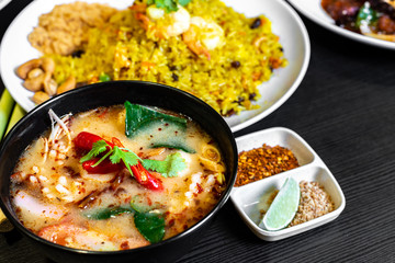 Tom Yum Soup or Tom Yam Kung is a traditional hot spicy sour soup, typical authentic dish in Thailand, usually cooked with shrimps. Pineapple fried rice in the background.