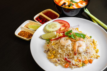 Thai seafood fried rice served with prawns, and a bowl of Tom Yum Soup in the background.