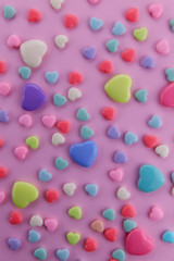 On a pink background there are many small and large hearts of different colors. Yellow, red, blue and green hearts on a pink background. Vertical, close-up. Valentine's day.