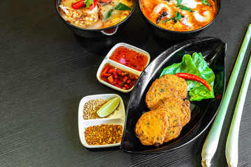 Spicy fried fish cake (Tod Mun Pla), a traditional Thailand appetizer is made with fresh fish paste, long beans, red curry paste and kaffir lime leaves. Authentic Thai Tom Yum soup & food on table.