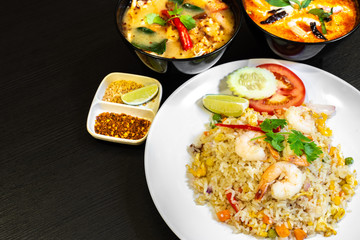 Thai seafood fried rice served with prawns in a white plate, and two bowls of Tom Yum Soup in the background.