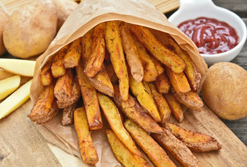 Homemade Crispy Seasoned French Fries..French fries  with spicy seasoning in brown paper bag on wooden broad.