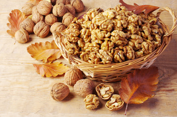 Walnut kernels in a wicker basket and inshell nuts on a wooden table. 