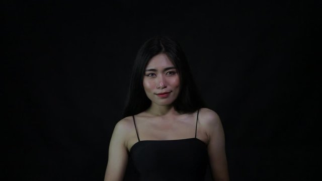 Asian Lady in black flick her long hair from back to see a cemera and smile on black background in studio
