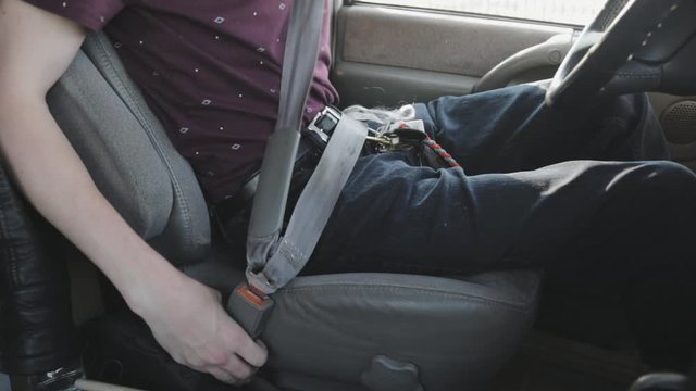 A young driver gets ready, fastening his seatbelt and getting comfortable in the car seat.