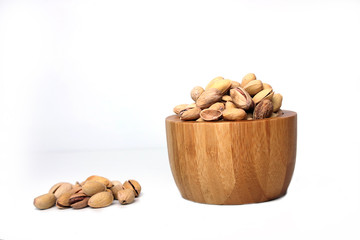 a pile of pistachio nuts next to a bowl of pistachio nuts isolated on white background. Horizontsl image