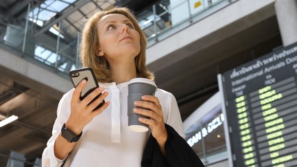 Young Business Woman With Coffee Using Smartphone At Airport Flight Timetable