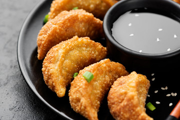 Asian dumplings fried Gyoza potstickers on black ceramic plate served with chopsticks and bowl of soy sesame sauce over black texture background. 