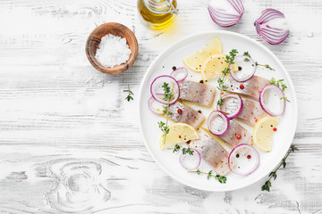 Salted herring with spices, lemon and red  onion rings on white wooden background . Marinated sliced fish. top view