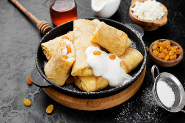 Thin pancakes or crepes stuffed with cottage cheese and raisins on black background. 