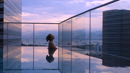 Young Female Traveler Relaxing In Rooftop Swimming Pool At Sunrise On Vacation