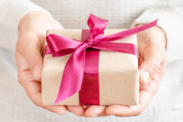 Close up of male hands holding small gift with purple ribbon bow.