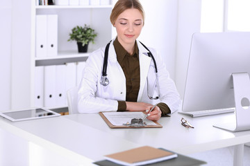 Obraz na płótnie Canvas Young woman doctor at work in hospital looking at desktop pc monitor. Physician controls medication history records and exam results. Medicine and healthcare concept
