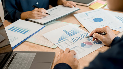 Concept of young business working at his coffee shop and using laptop, holding smartphone in hand discussing the charts and graphs showing the results of their successful teamwork.