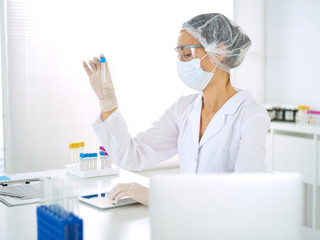 Professional female scientist in protective eyeglasses researching tube with reagents in...