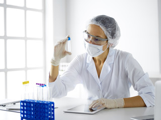Professional female scientist in protective eyeglasses researching tube with reagents in...
